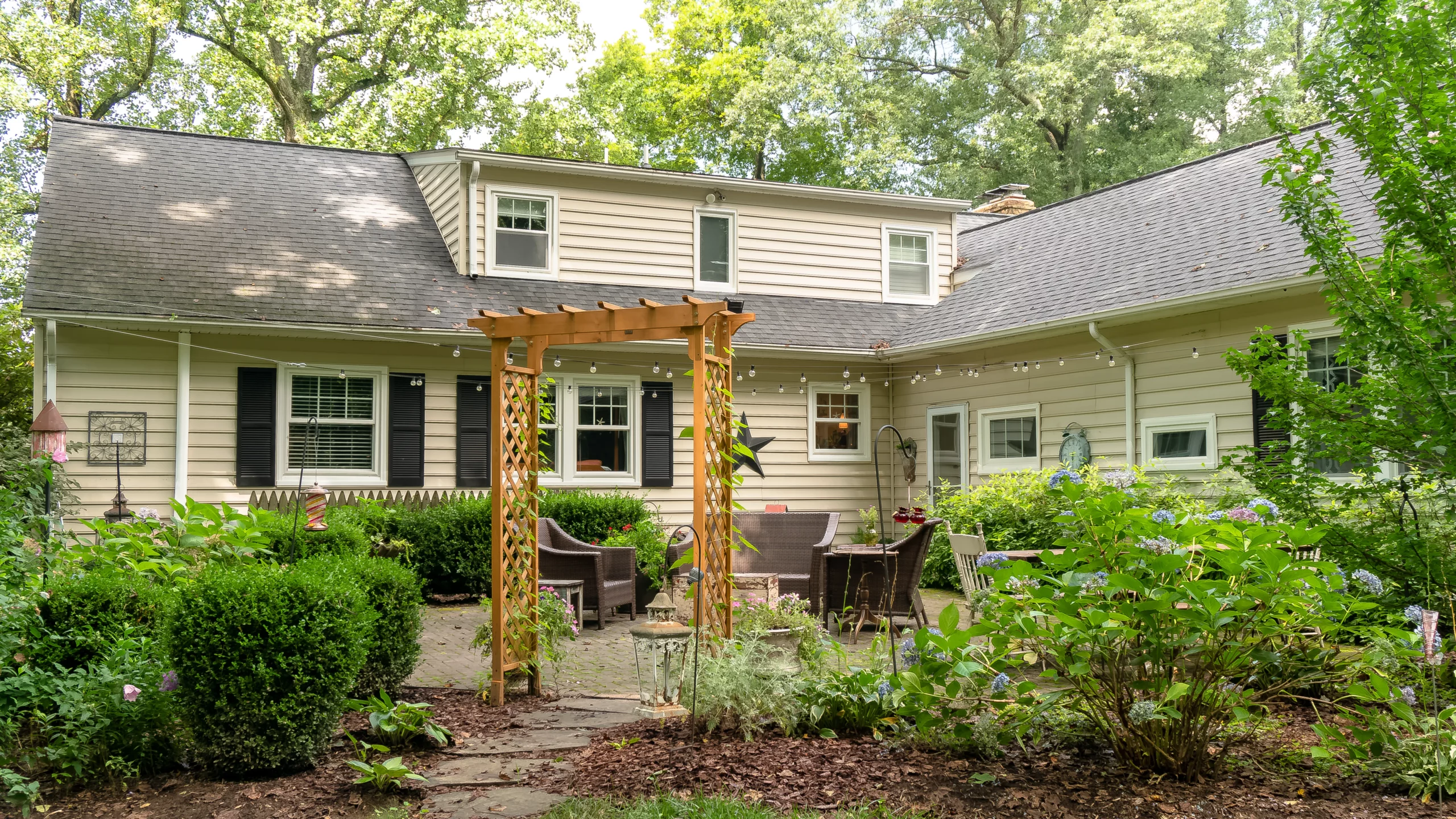 A new asphalt shingle roof on a home with beige vinyl siding with a lush garden in front of the home